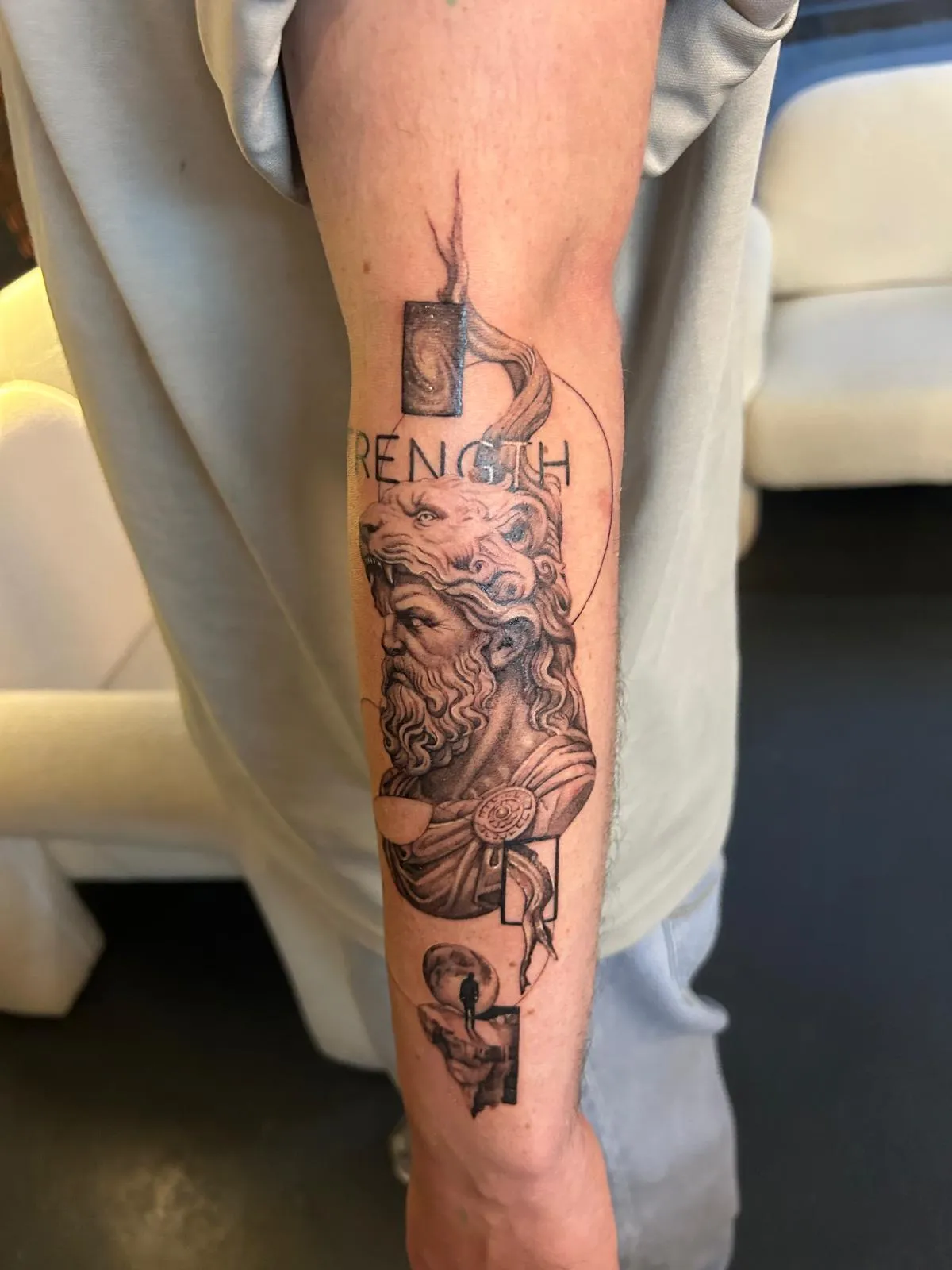 Unterarm-Tattoo mit Zeus-Büste, Säulen und dem Wort STRENGTH in Black and Grey